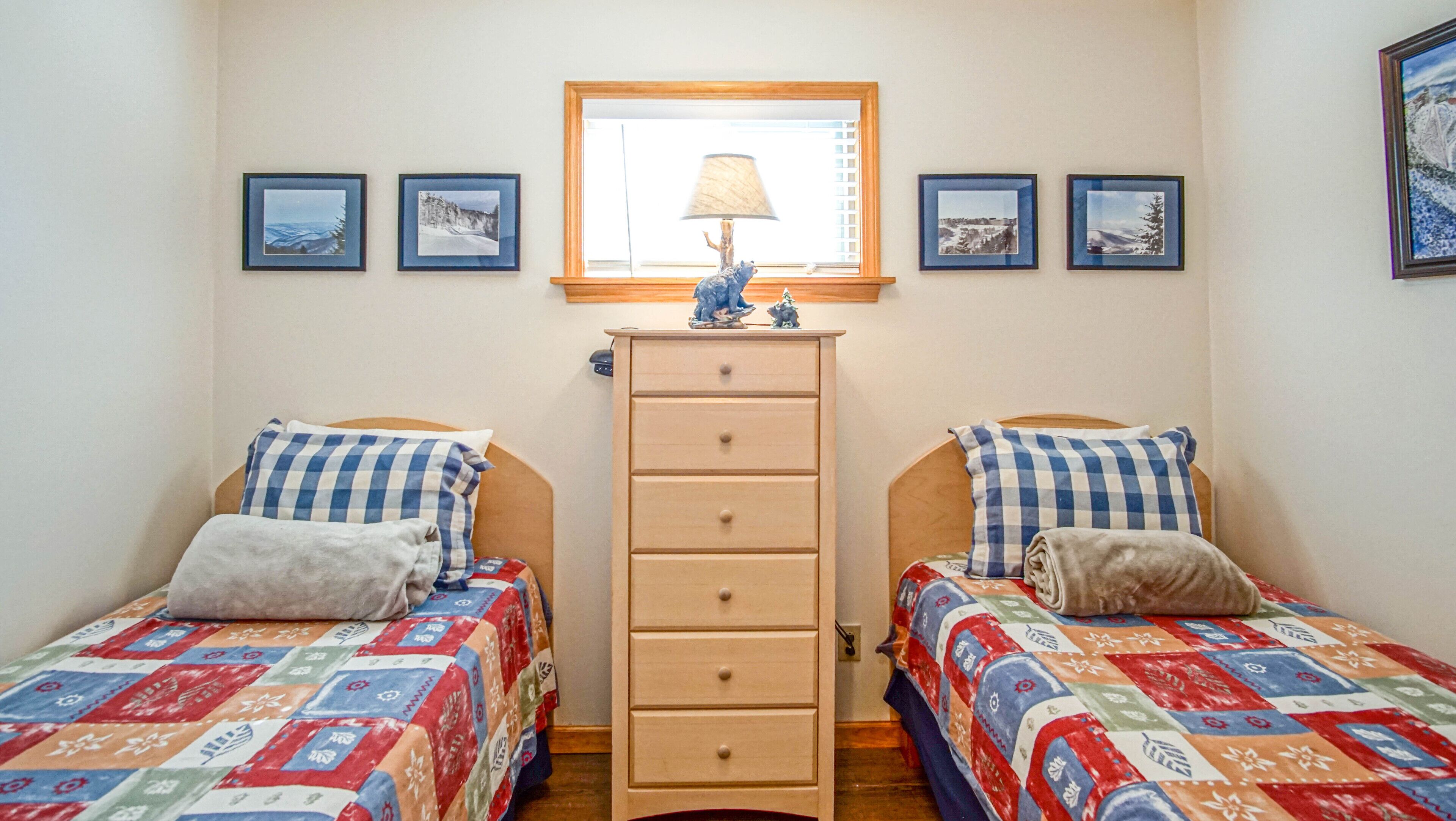A bedroom with two single beds, a dresser, and a window with a lamp.