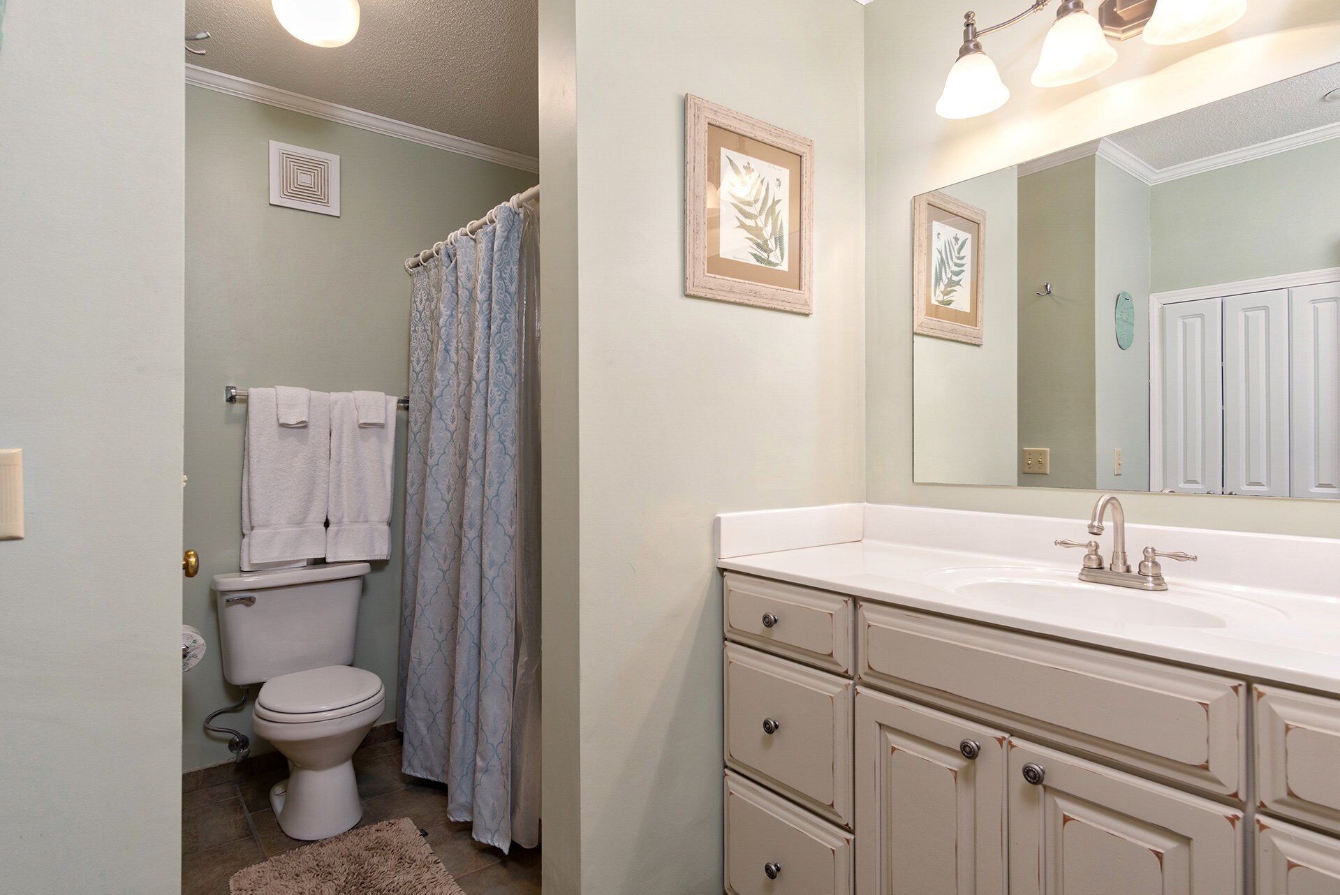 A bathroom with a toilet, a shower with a curtain, a sink with a mirror, and a cabinet.