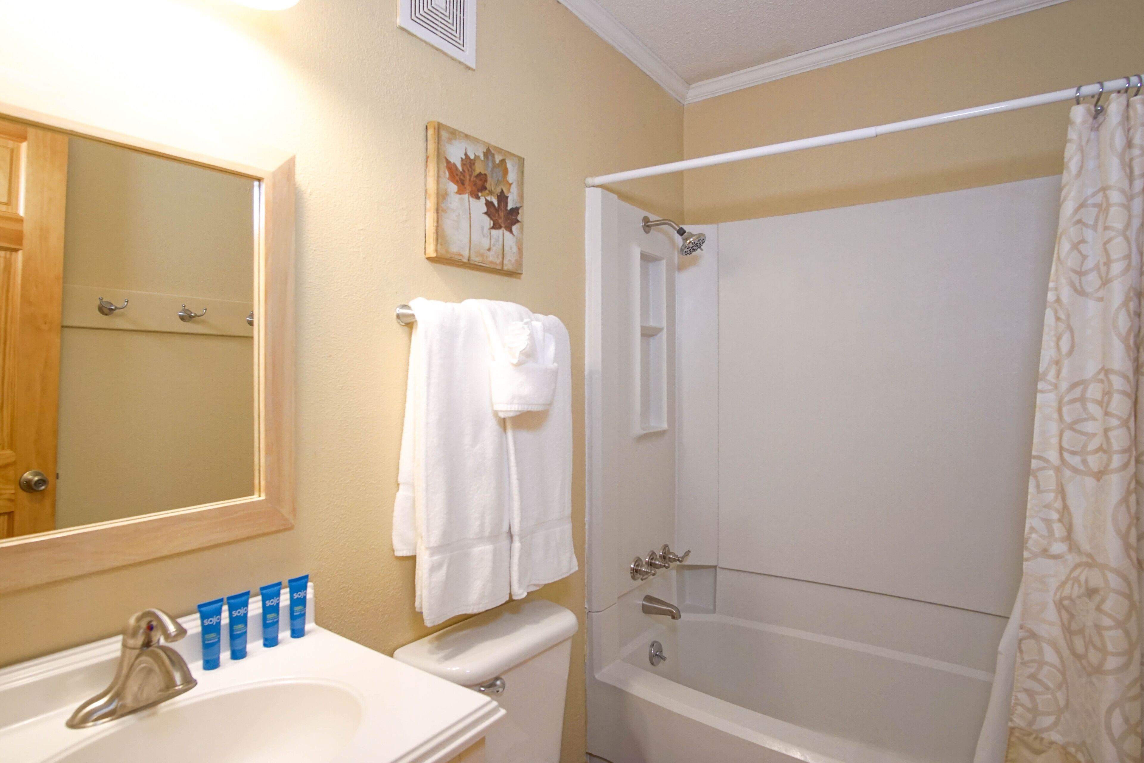 A bathroom with a sink, toilet, and bathtub. There are towels hanging on the wall and a shower curtain.