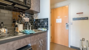 A modern kitchen with a microwave, stove, and sink. There are cabinets, a tiled backsplash, and a wooden door. - Expedition Station #120: Snowshoe's Premier Slopeside Junior Studio Accommodations (Snowshoe)