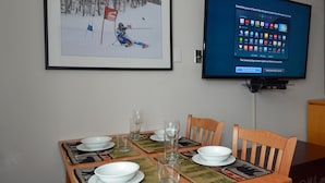 A dining area with a table set for four, a framed picture of a skier, and a TV displaying Samsung Apps. - Expedition Station #120: Snowshoe's Premier Slopeside Junior Studio Accommodations (Snowshoe)