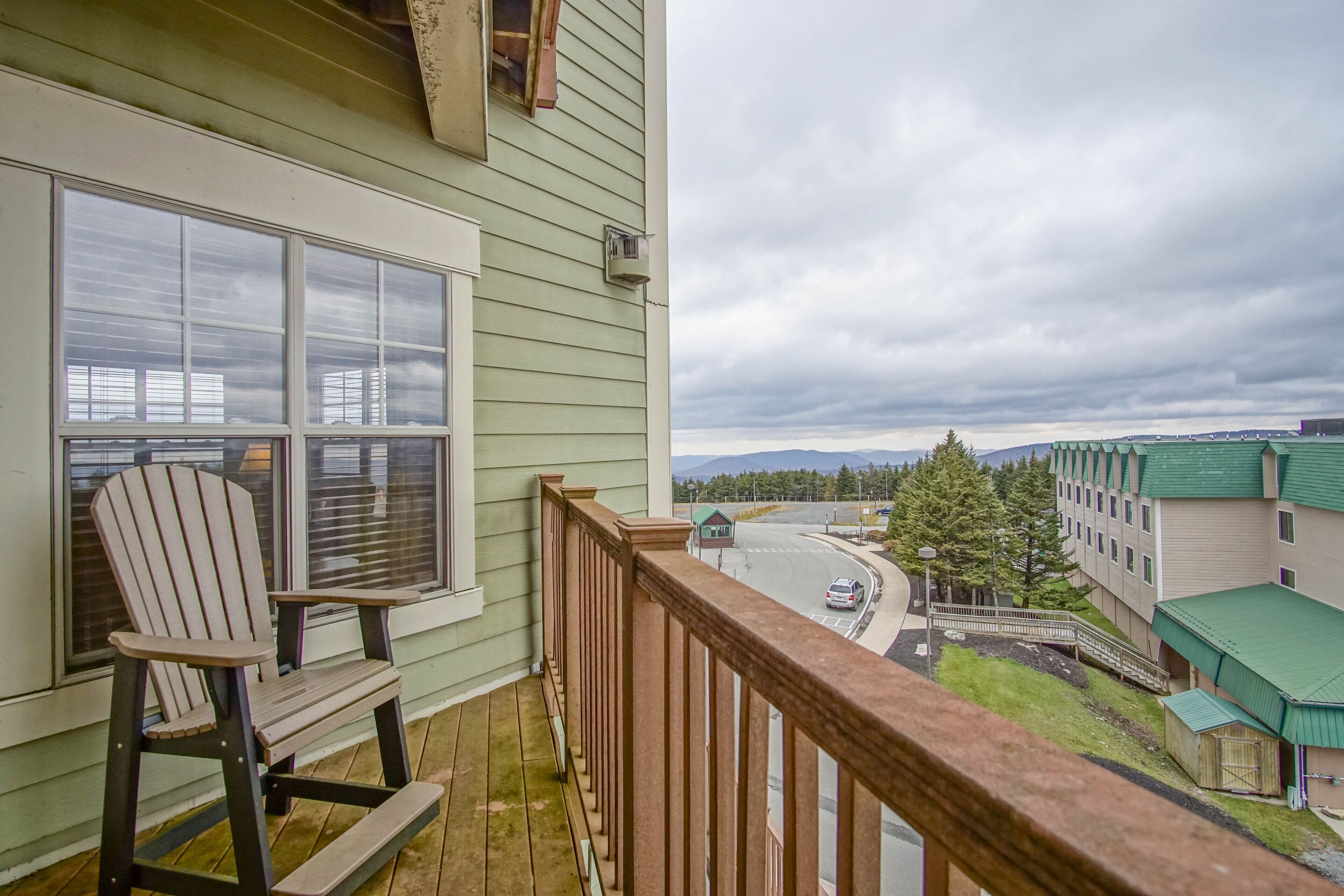 A balcony with a rocking chair, a view of a road, and buildings in the background.
