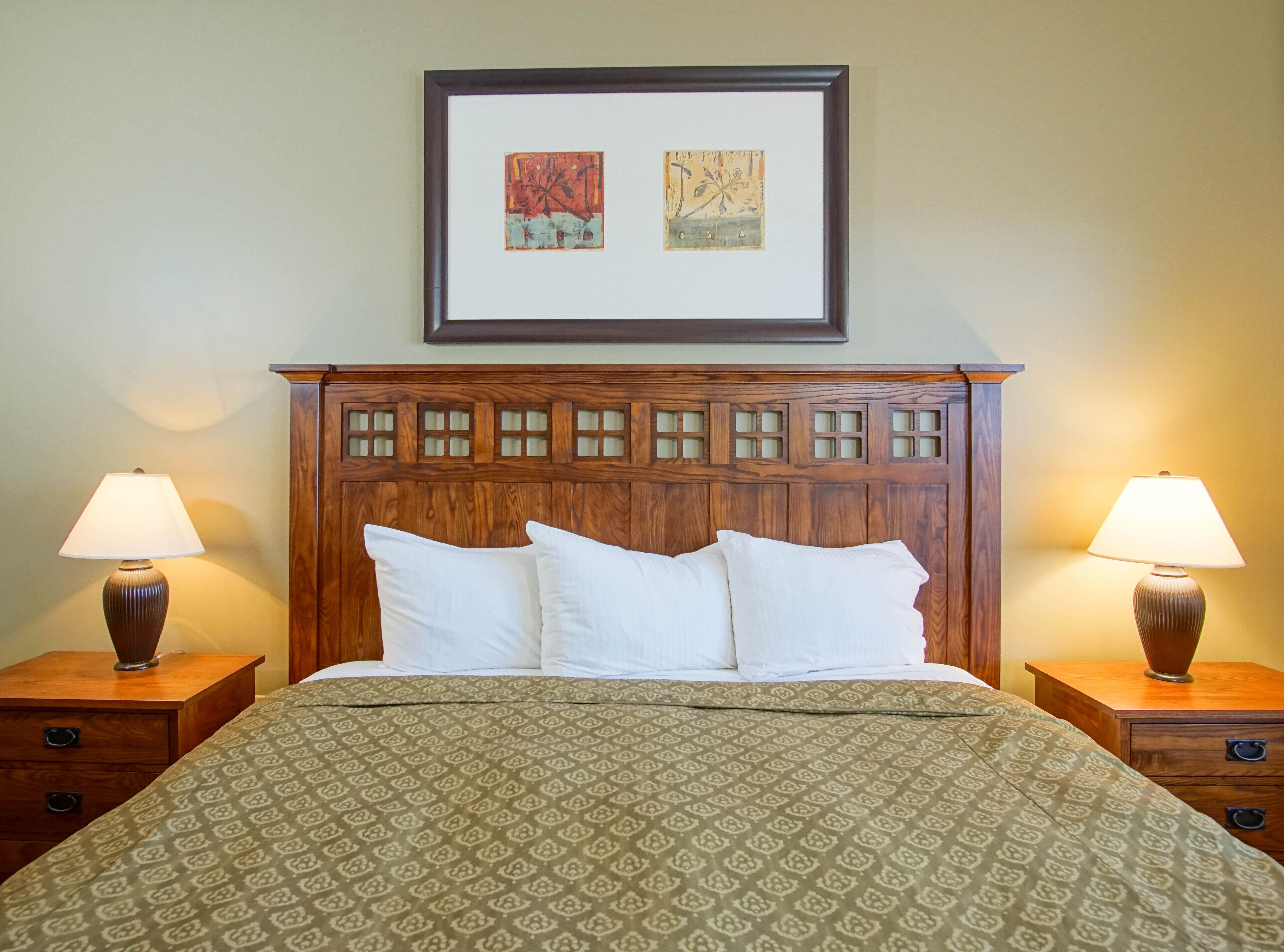 A neatly made bed with a patterned bedspread, two bedside lamps, and a framed artwork above the headboard.