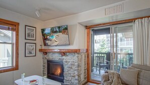 A cozy living room with a stone fireplace, a television mounted above it, and a large window overlooking a pool and outdoor area. - Rimfire 342: Memory Maker, Walk to Shops, Slope Side (Snowshoe)