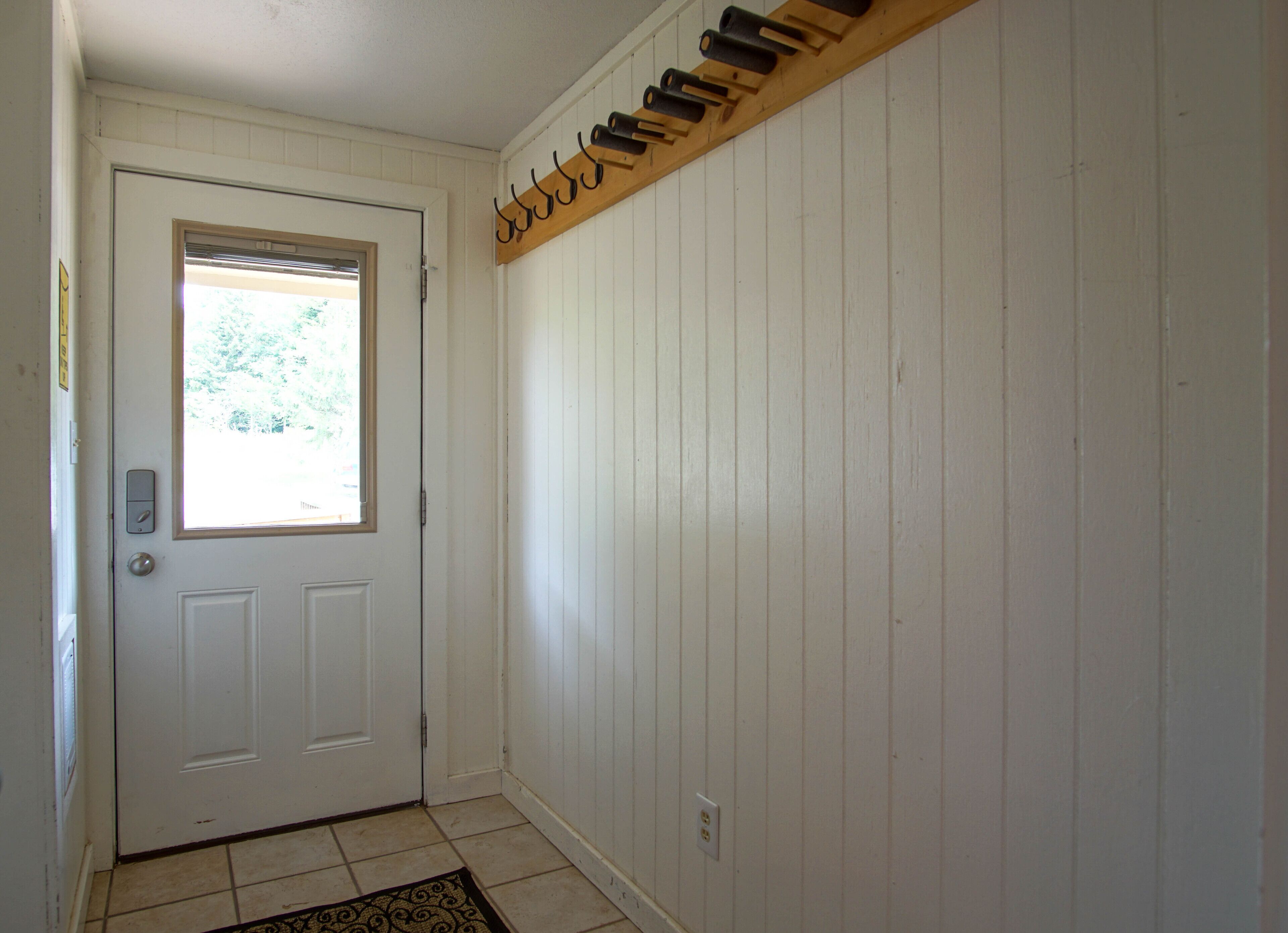 A hallway with a white door, a window, and a wooden coat rack.