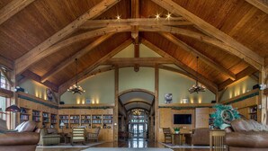 A spacious library with high ceilings and wooden beams, featuring bookshelves, leather sofas, and a large arched doorway. - Soaring Eagle #405: 3 Br Location! Slope Side, Hot Tub (Snowshoe)