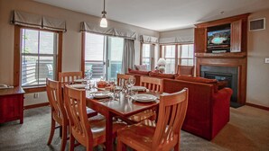 Un comedor con una mesa de madera preparada para cuatro, un sofá rojo y un televisor sobre la chimenea.