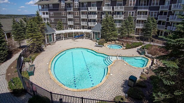 Un hotel con una amplia piscina exterior, un patio cubierto y un edificio de varios pisos con balcones.
