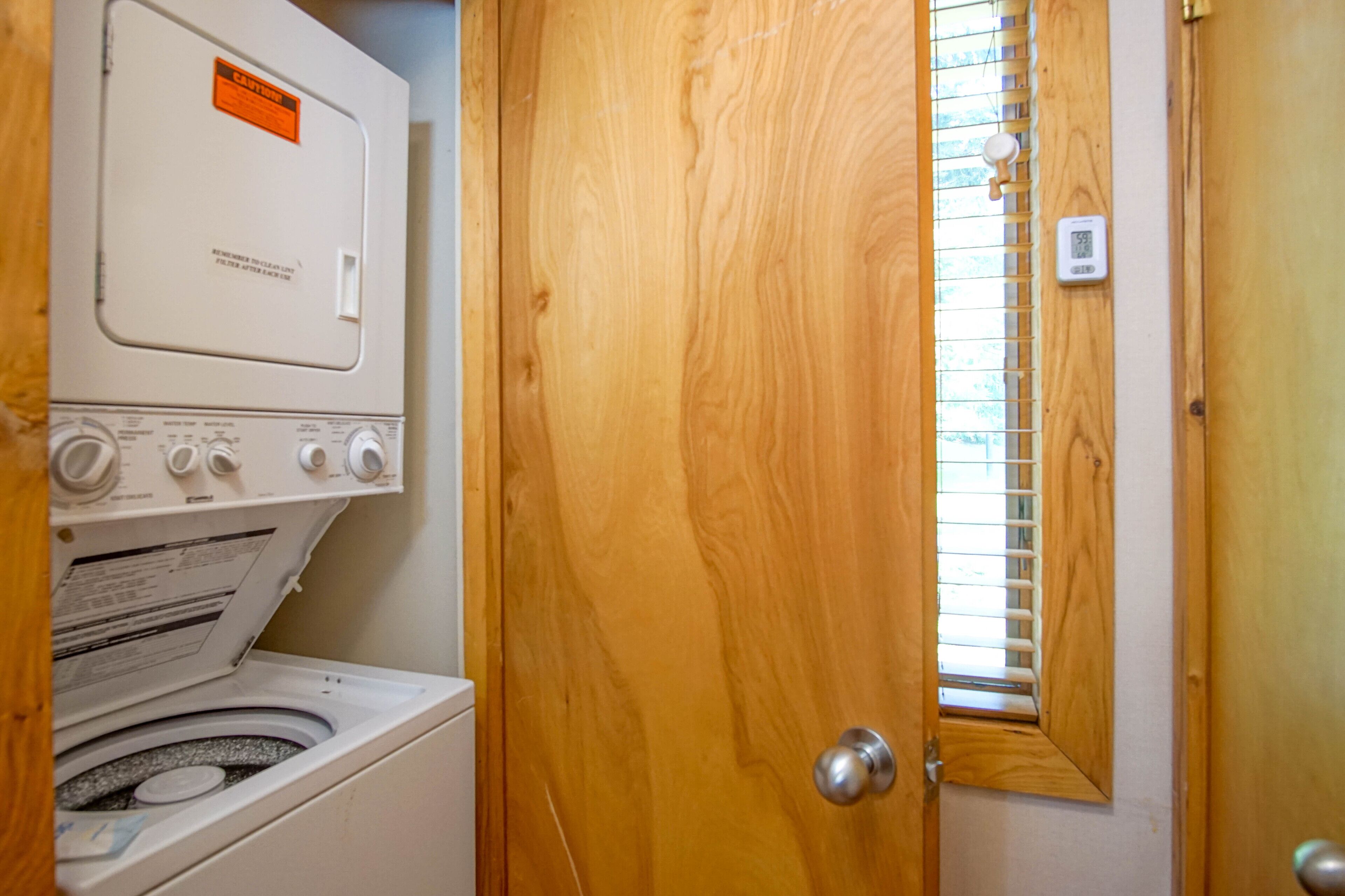 A laundry room with a front-loading washer and dryer, wooden doors, and a window with blinds.