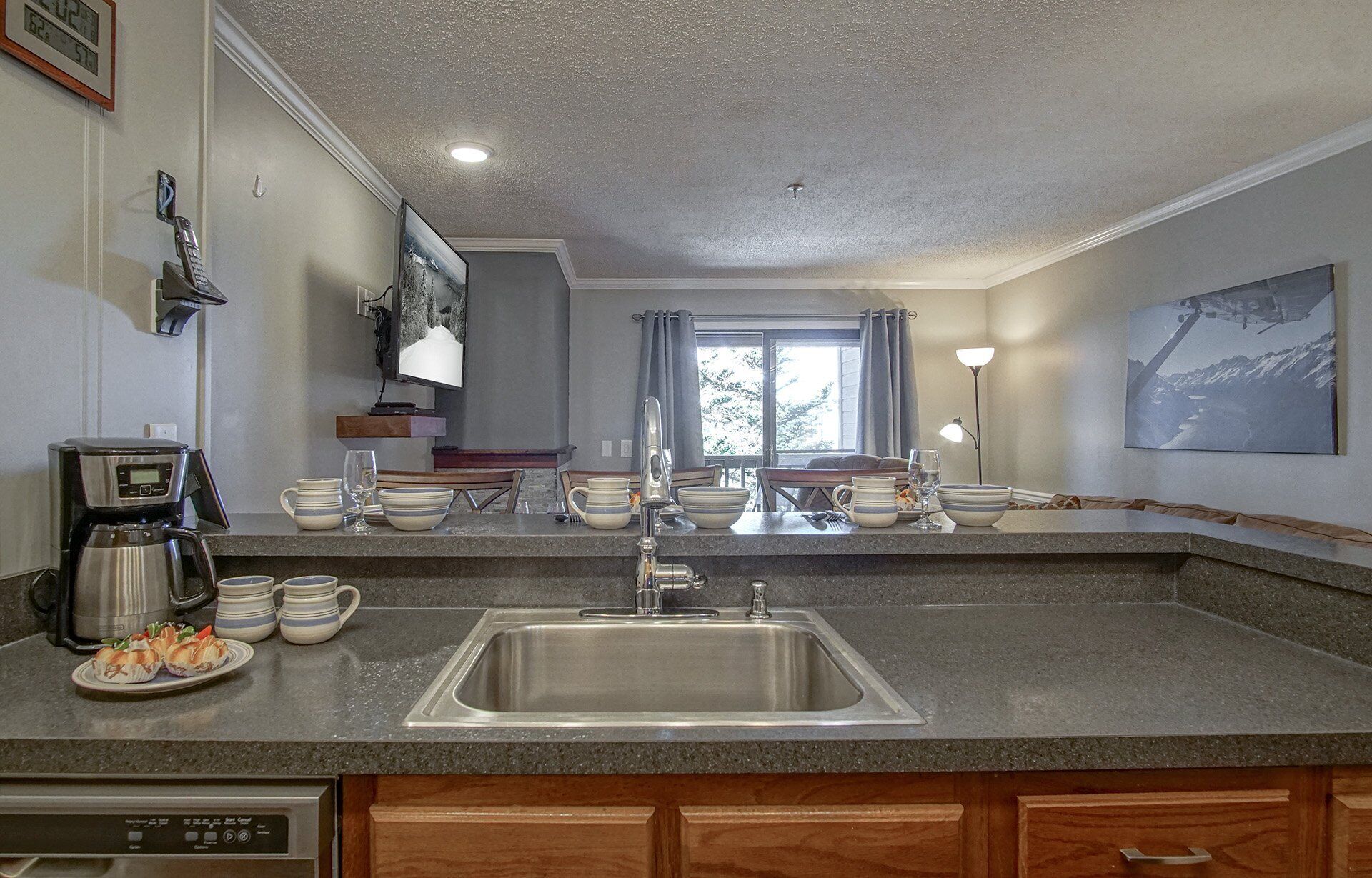 A kitchen with a granite countertop, stainless steel sink, and wooden cabinets. There is a coffee maker, a toaster, and a microwave on the counter.