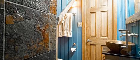 A bathroom with a stone wall, a wooden door, a white toilet, and a wooden vanity with a sink.