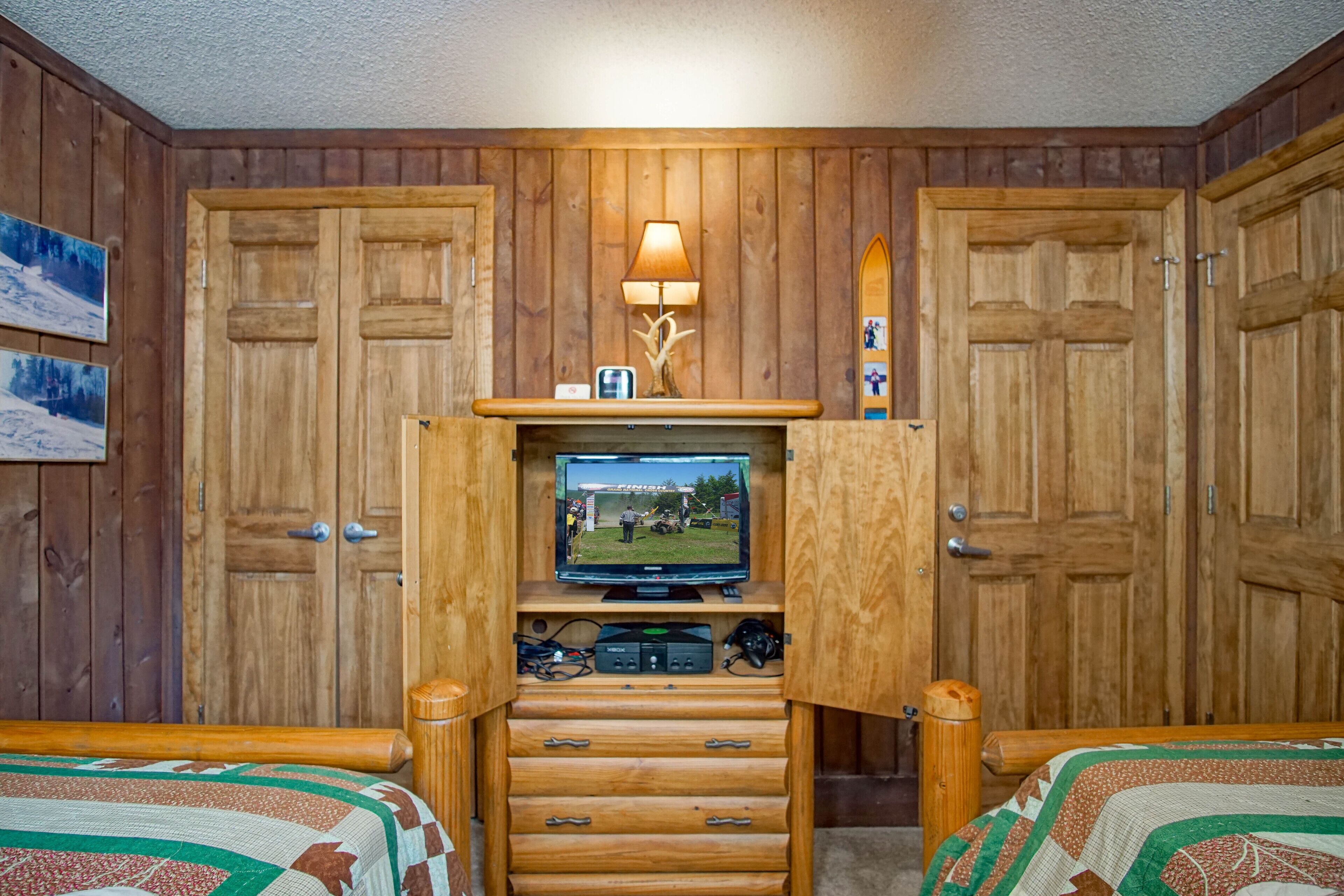 Una habitación acogedora con paredes de madera y un televisor sobre un mueble de madera. Hay dos camas con colchas estampadas.