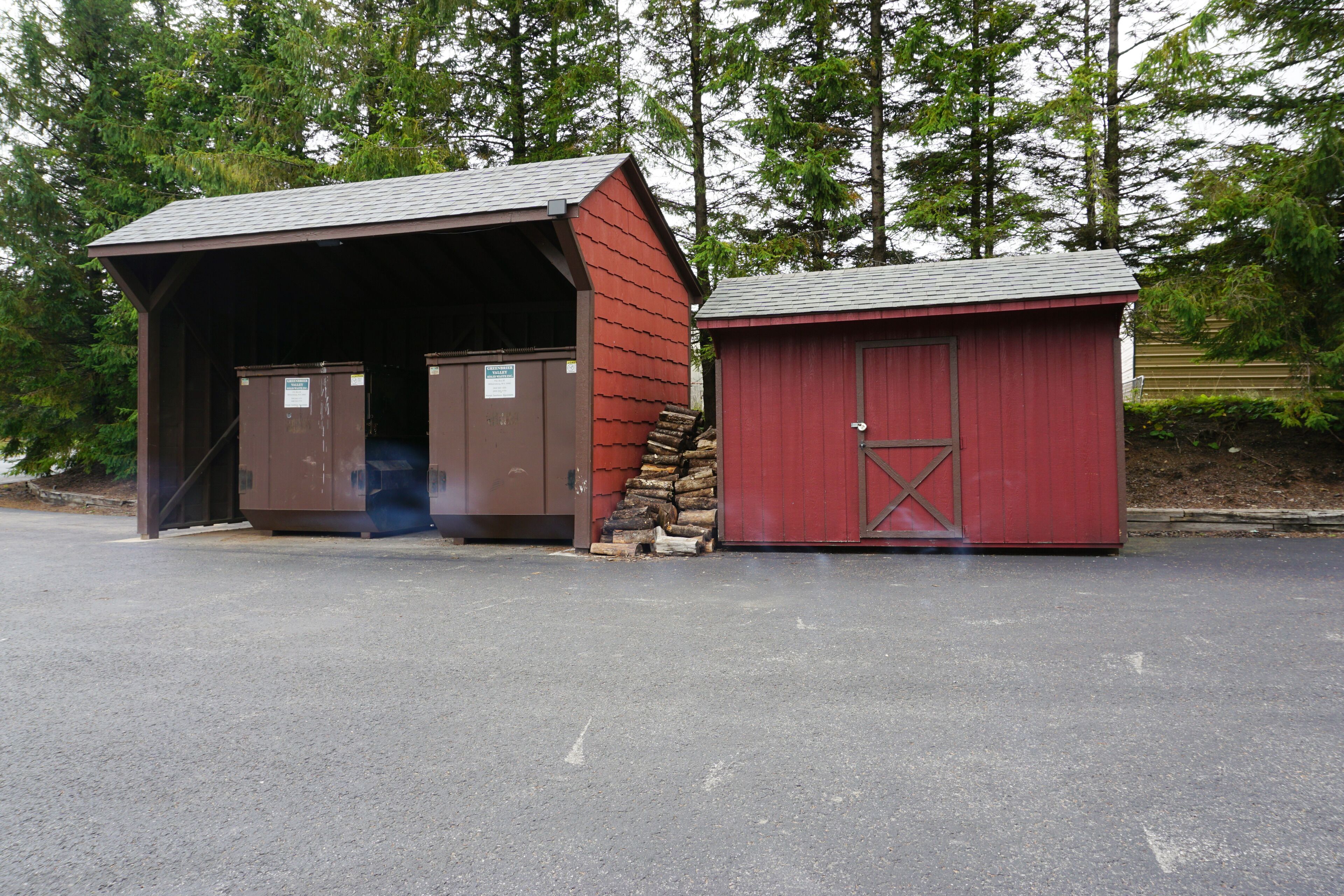 A red and brown building with a covered entrance and a stack of firewood beside it.