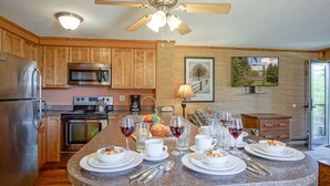 A kitchen with wooden cabinets, stainless steel appliances, a granite countertop, and a dining area set for a meal. - Powderidge 1 Hideaway Slope Side (Snowshoe)