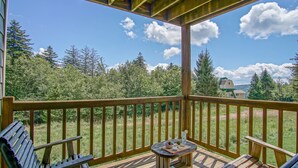 A wooden deck with a table and chairs, overlooking a grassy area with trees and a distant building. - Powderidge 1 Hideaway Slope Side (Snowshoe)
