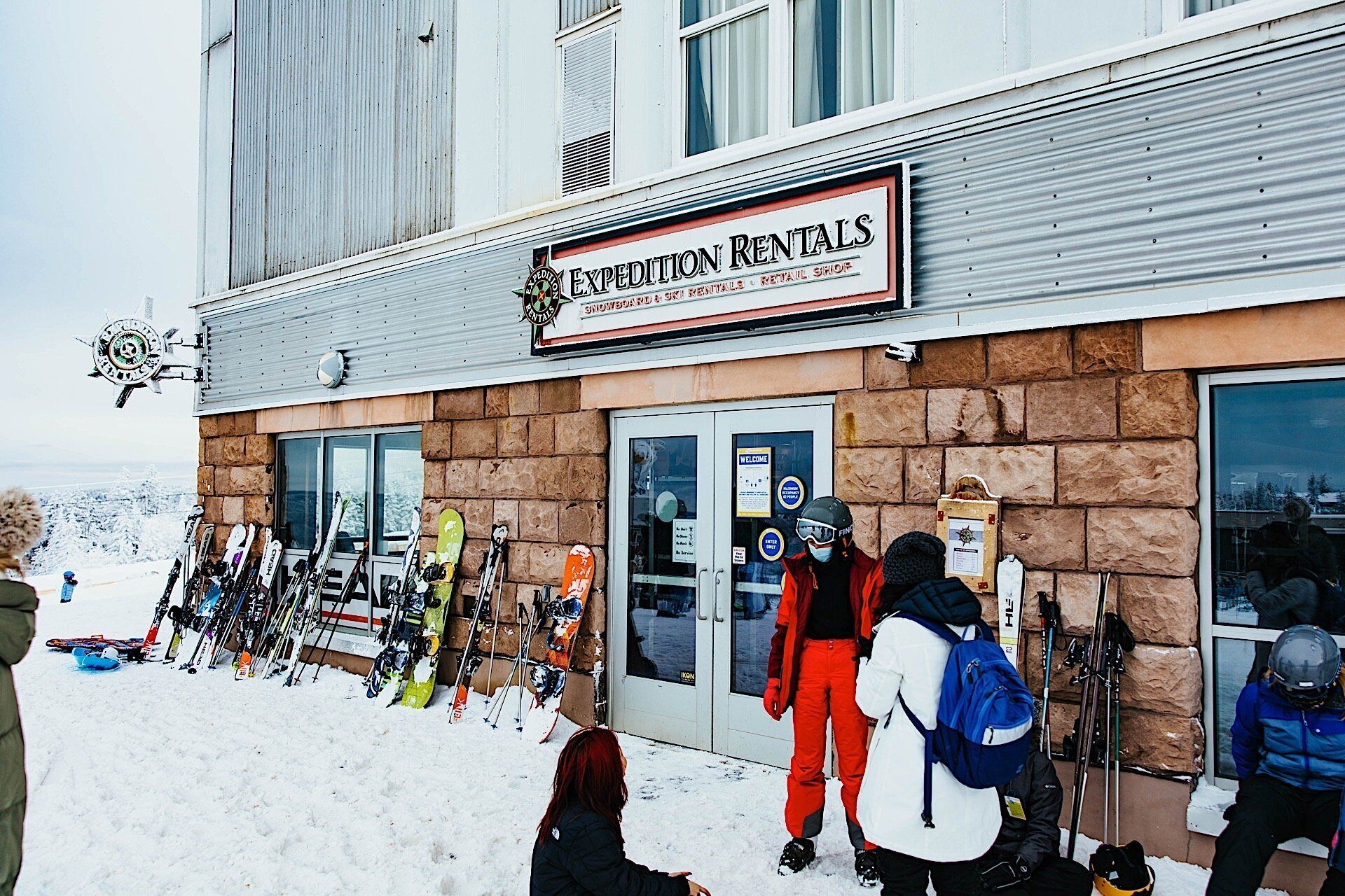 A building with a sign for 'Expedition Rentals' and a row of skis outside.