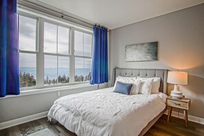 A bedroom with a large window, a bed with white bedding, a nightstand with a lamp, and a painting on the wall. - Slope Side! 2 Bed 2 Bath Expedition Station 201 (Snowshoe)