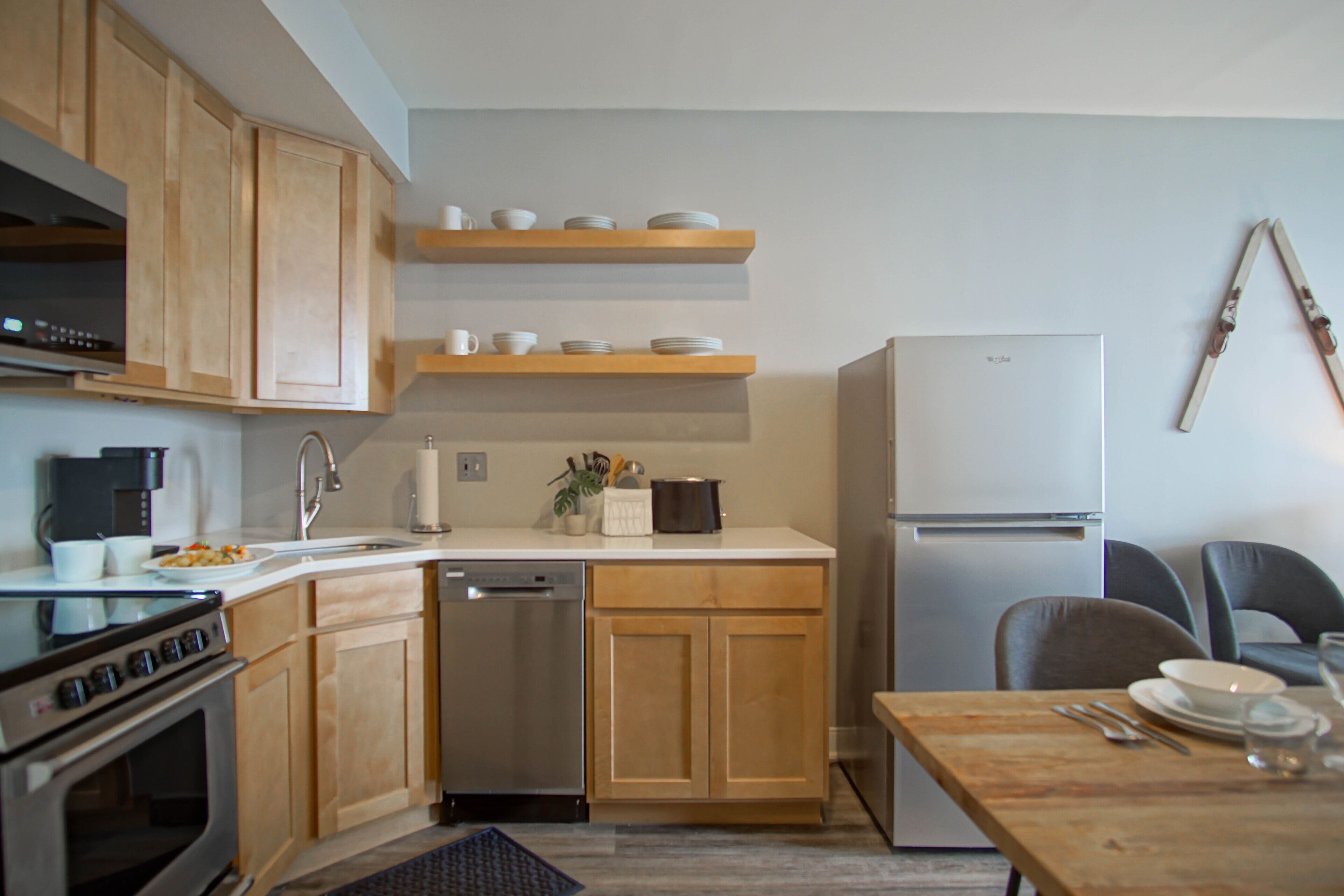 A modern kitchen with wooden cabinets, stainless steel appliances, and a dining area with a table set for two.