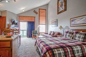 Quarto com cama grande, uma cadeira, escrivaninha e janela com persianas.