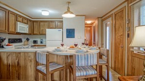 A kitchen with wooden cabinets, a white refrigerator, a microwave, a dining table with chairs, and a hanging light fixture. - Powderidge 60: Slope Side, Fireplace, Spacious Deck (Snowshoe)