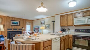 A kitchen with wooden cabinets, a microwave, an oven, and a dining area with a round table and chairs. - Powderidge 60: Slope Side, Fireplace, Spacious Deck (Snowshoe)
