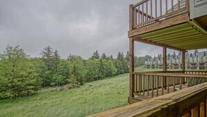 A wooden deck with a view of a grassy hillside and trees. - Powderidge 60: Slope Side, Fireplace, Spacious Deck (Snowshoe)