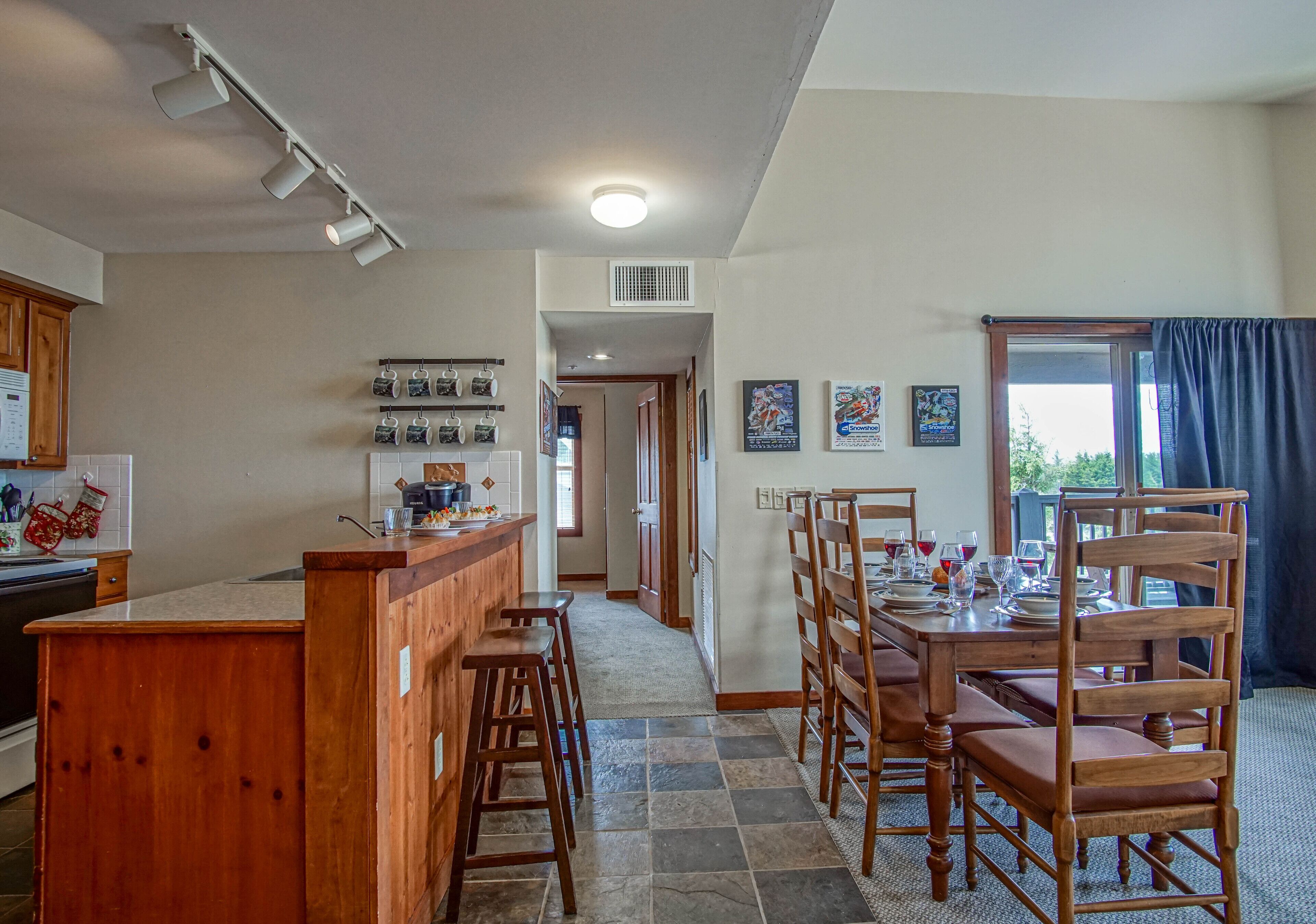 A kitchen with a wooden island, bar stools, and a dining area with wooden chairs and a table set for four.