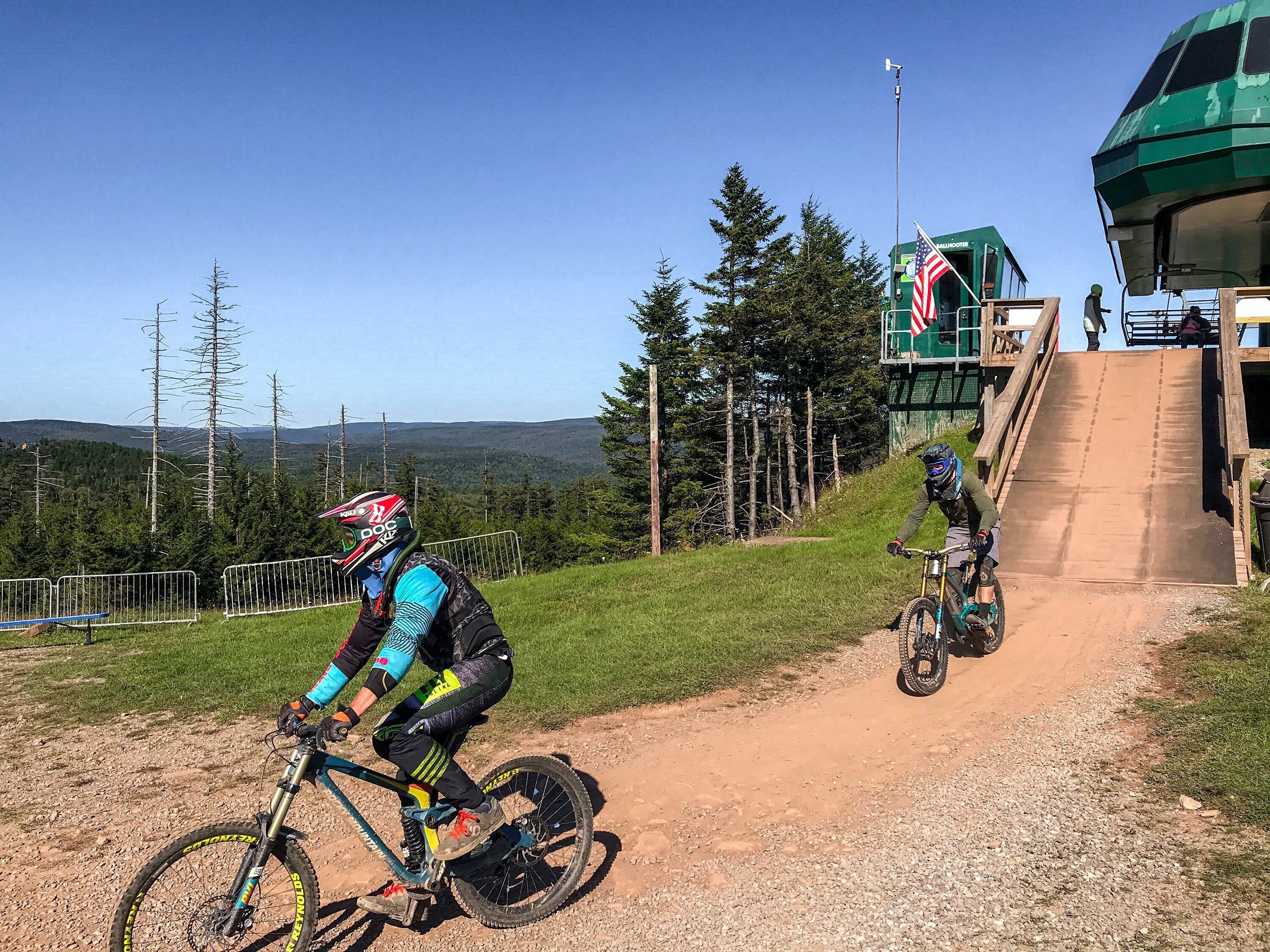 Un sendero para bicicletas de montaña con una rampa de madera y un edificio verde al fondo.