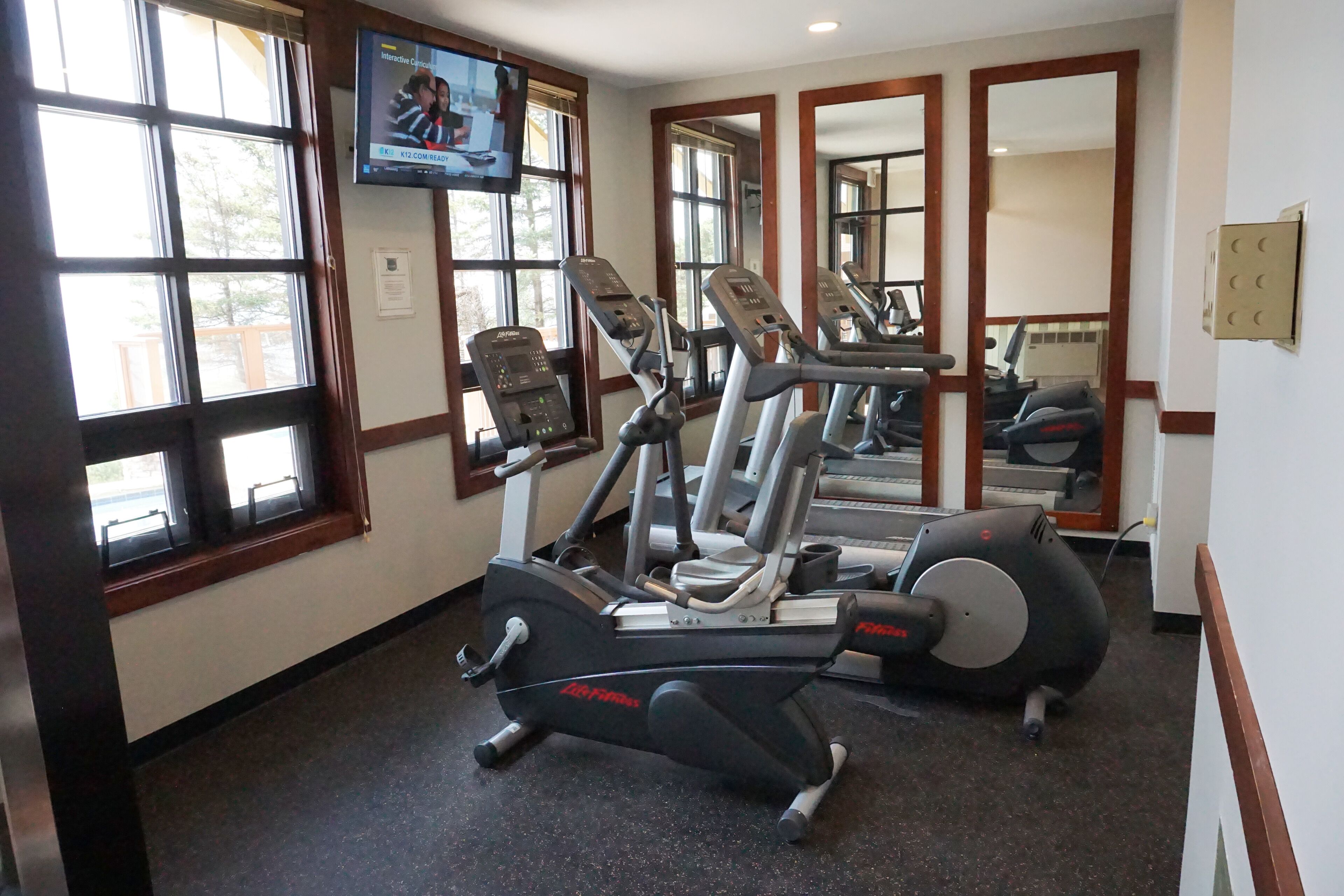 A gym with cardio machines, mirrors, and a TV screen.