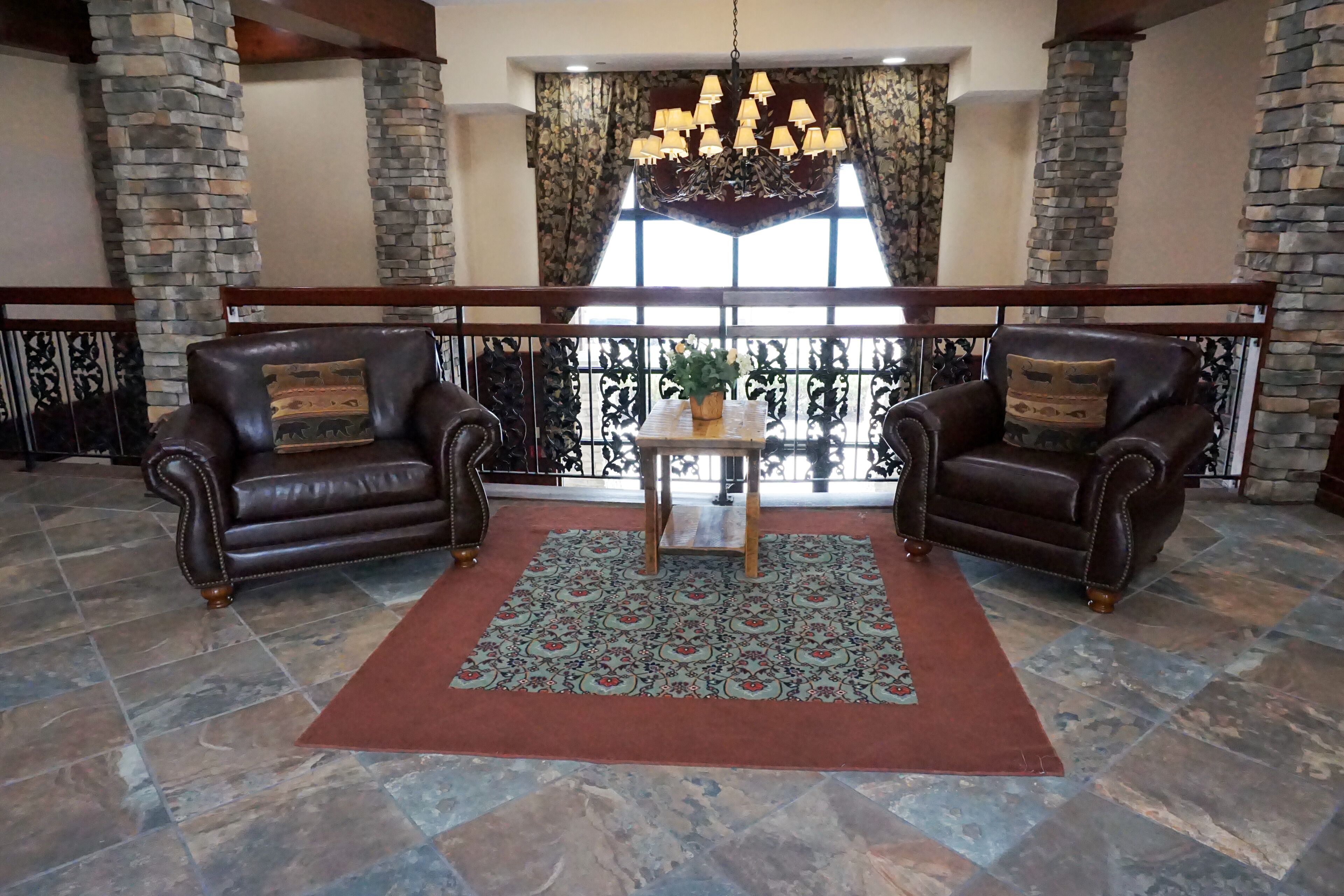 Un hall d’entrée spacieux, agrémenté de piliers en pierre, de fauteuils en cuir, d’un tapis à motifs et d’un lustre.