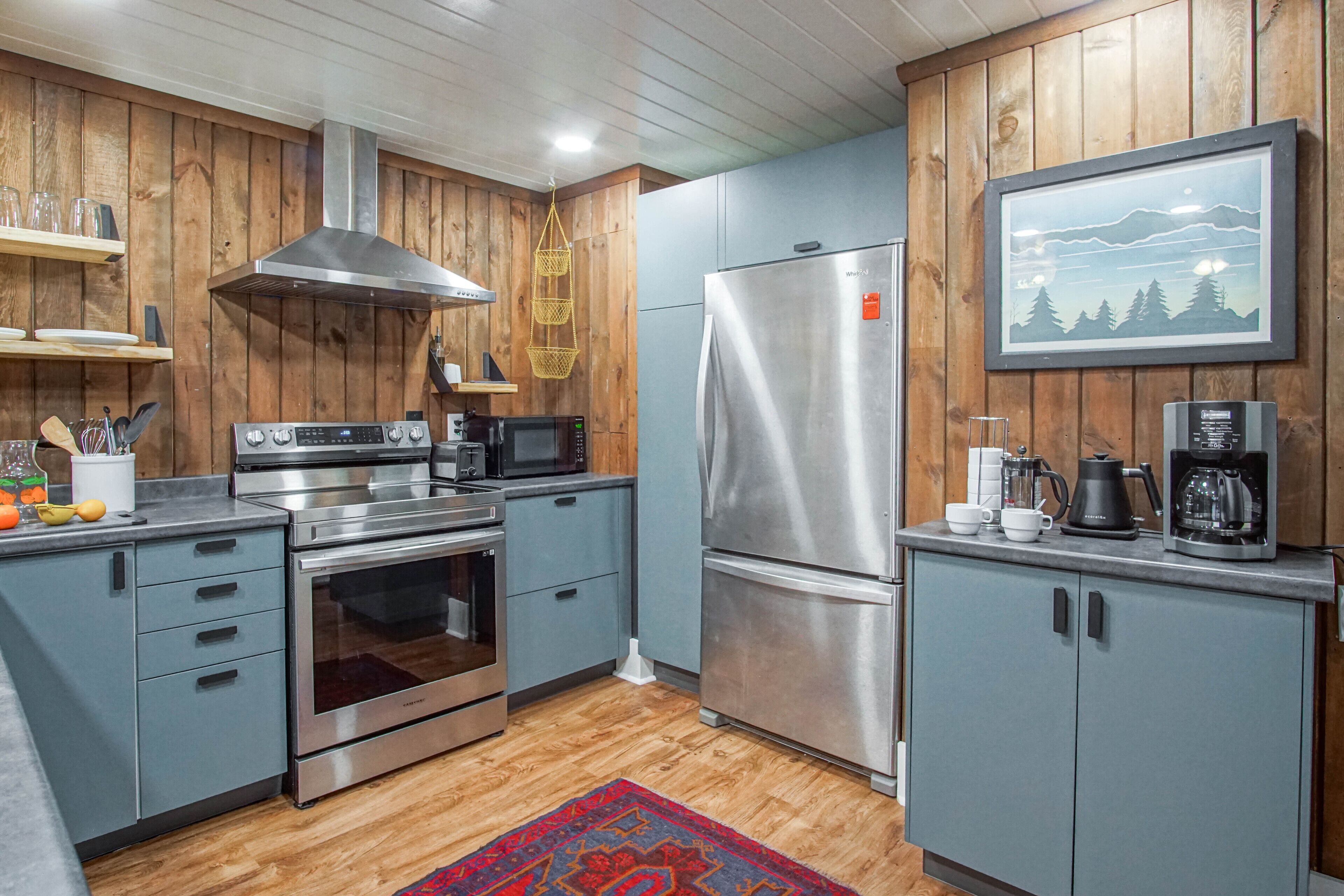 A modern kitchen with wooden paneling, stainless steel appliances, and a mounted picture of a mountain landscape.