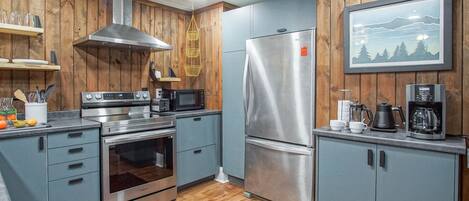 A modern kitchen with wooden paneling, stainless steel appliances, and a mounted picture of a mountain landscape.