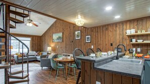 A modern kitchen with wooden walls, a dining area with green chairs, and a staircase leading to an upper level. - 2 Br: Wabasso 5: 2br, 2 Bath (Snowshoe)
