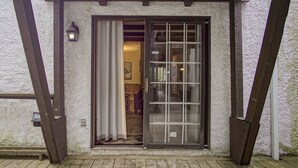 A wooden deck leading to a building with a sliding glass door, a small outdoor light fixture, and a visible interior with a chair and a table. - Whistlepunk #31: 2 Bedrooms, 2 Bath: Slope Side, Central Location. Wood Fireplace (Snowshoe)