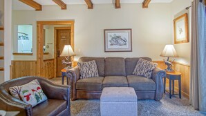 A cozy living room with a sofa, armchair, and ottoman, wooden beams on the ceiling, and a framed picture on the wall. - Whistlepunk #31: 2 Bedrooms, 2 Bath: Slope Side, Central Location. Wood Fireplace (Snowshoe)