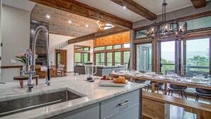 A modern kitchen with a large island, wooden beams, and large windows offering a view of the outdoors. - 5 Br: Cupp Runneth Over - Luxurious Retreat Nestled 9.7 Miles From Snowshoe (Slaty Fork)