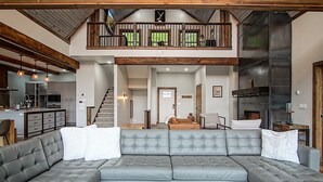 A spacious living area with a large sectional sofa, a kitchen with modern appliances, a staircase leading to an upper level, and a fireplace. - 5 Br: Cupp Runneth Over - Luxurious Retreat Nestled 9.7 Miles From Snowshoe (Slaty Fork)