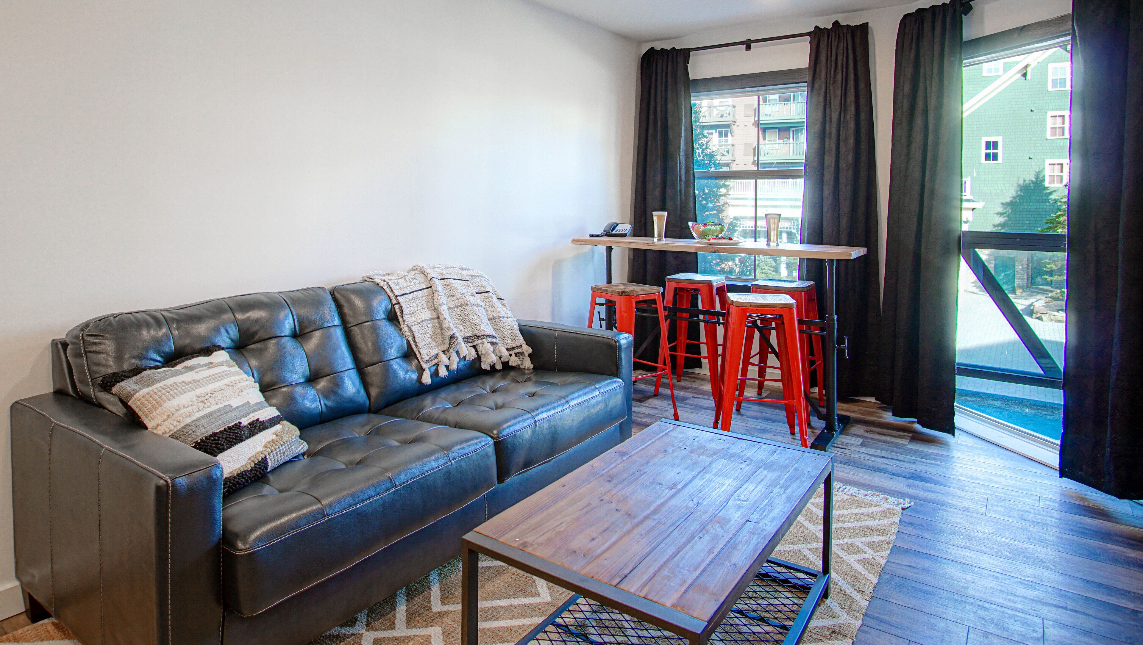 A modern living room with a leather sofa, a wooden coffee table, and red bar stools.
