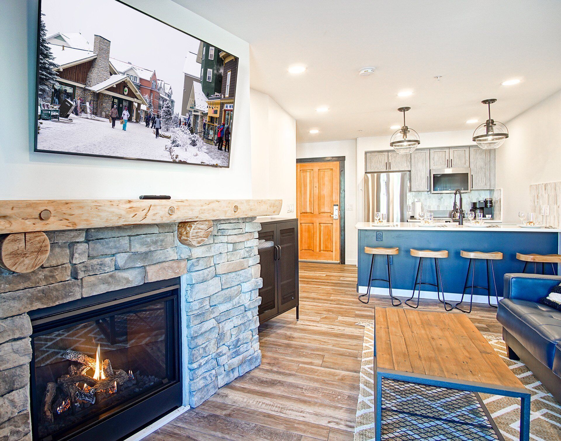 A modern kitchen with a stone fireplace, wooden bar stools, and a blue accent wall.