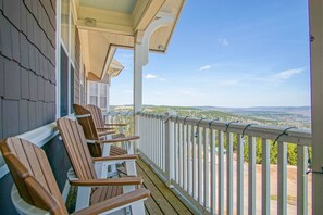 Une terrasse en bois avec des fauteuils Adirondack, une balustrade blanche et une vue sur un paysage vallonné.