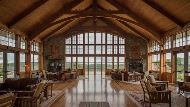 Amplia habitación con techos altos y ventanas grandes, que incluye chimenea, muebles de madera y vistas al exterior.