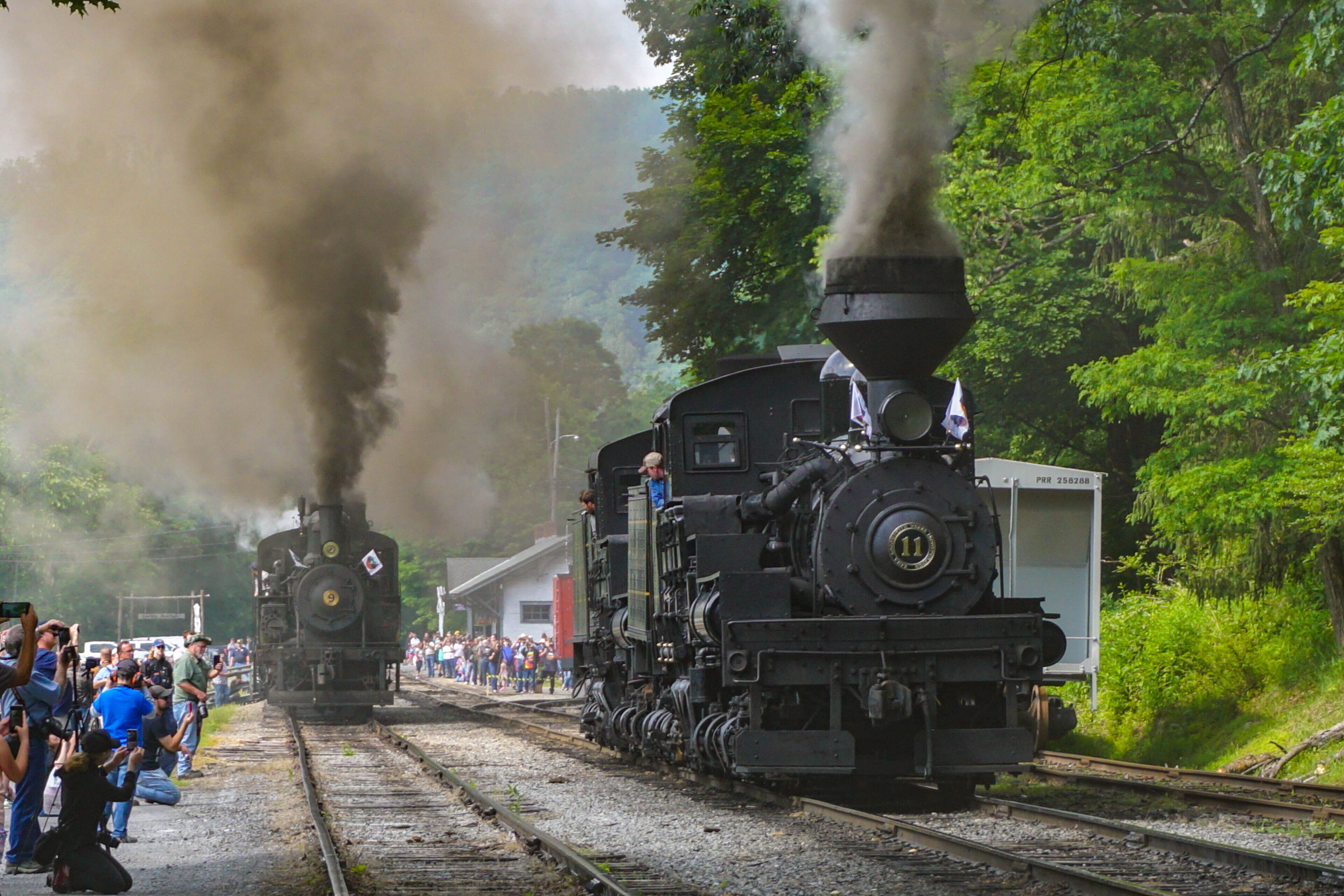 A steam locomotive with a large chimney emitting smoke, surrounded by a crowd of people.