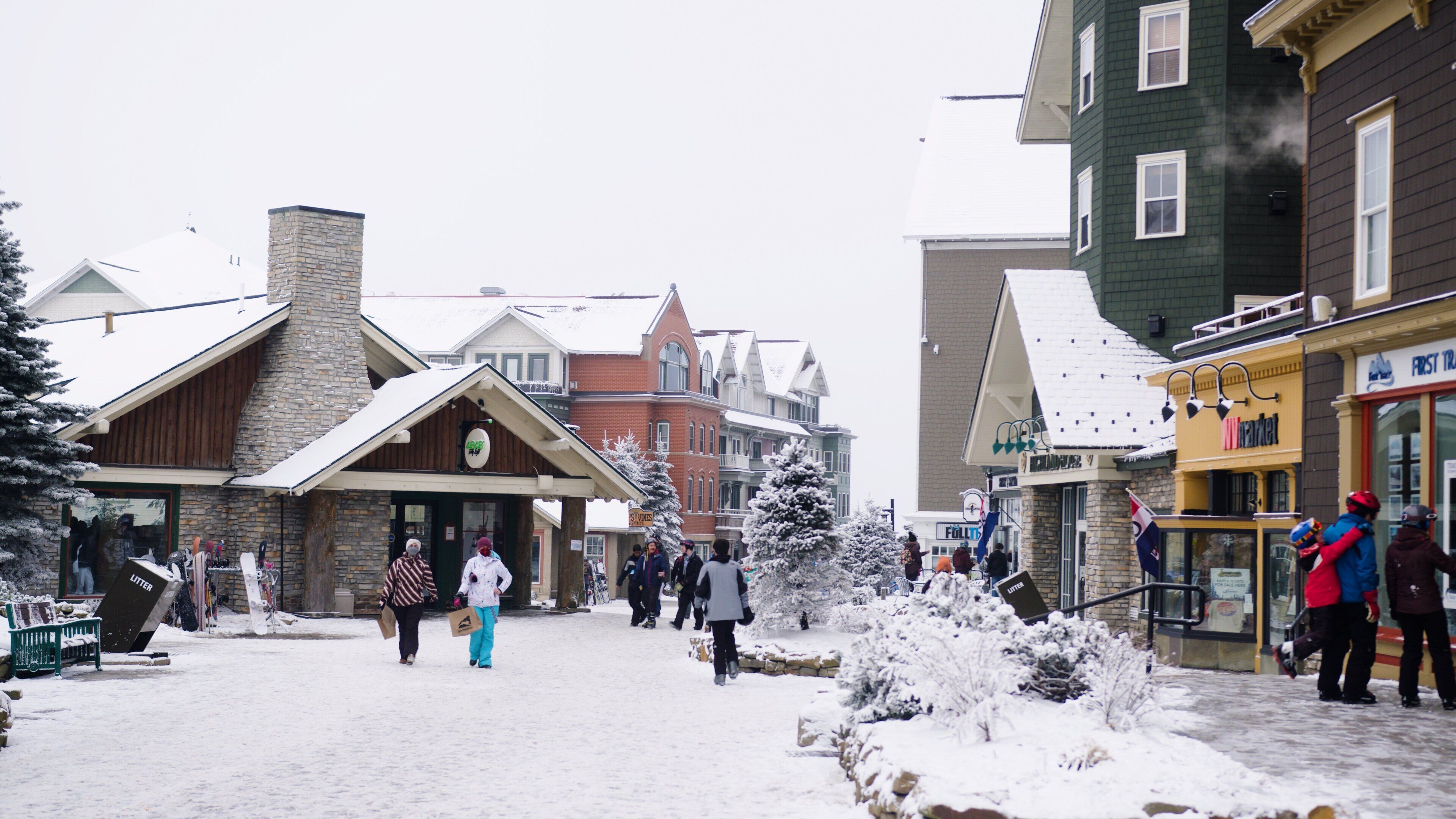 A snowy town square with buildings, including a market and a store with a sign that reads "FIRST TRAVEL".