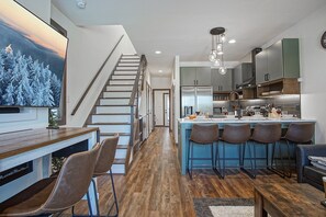 A modern kitchen with a central island, bar stools, and a staircase leading to another level. - 3 Br: Sanctuary 185 at Snowshoe (Snowshoe)