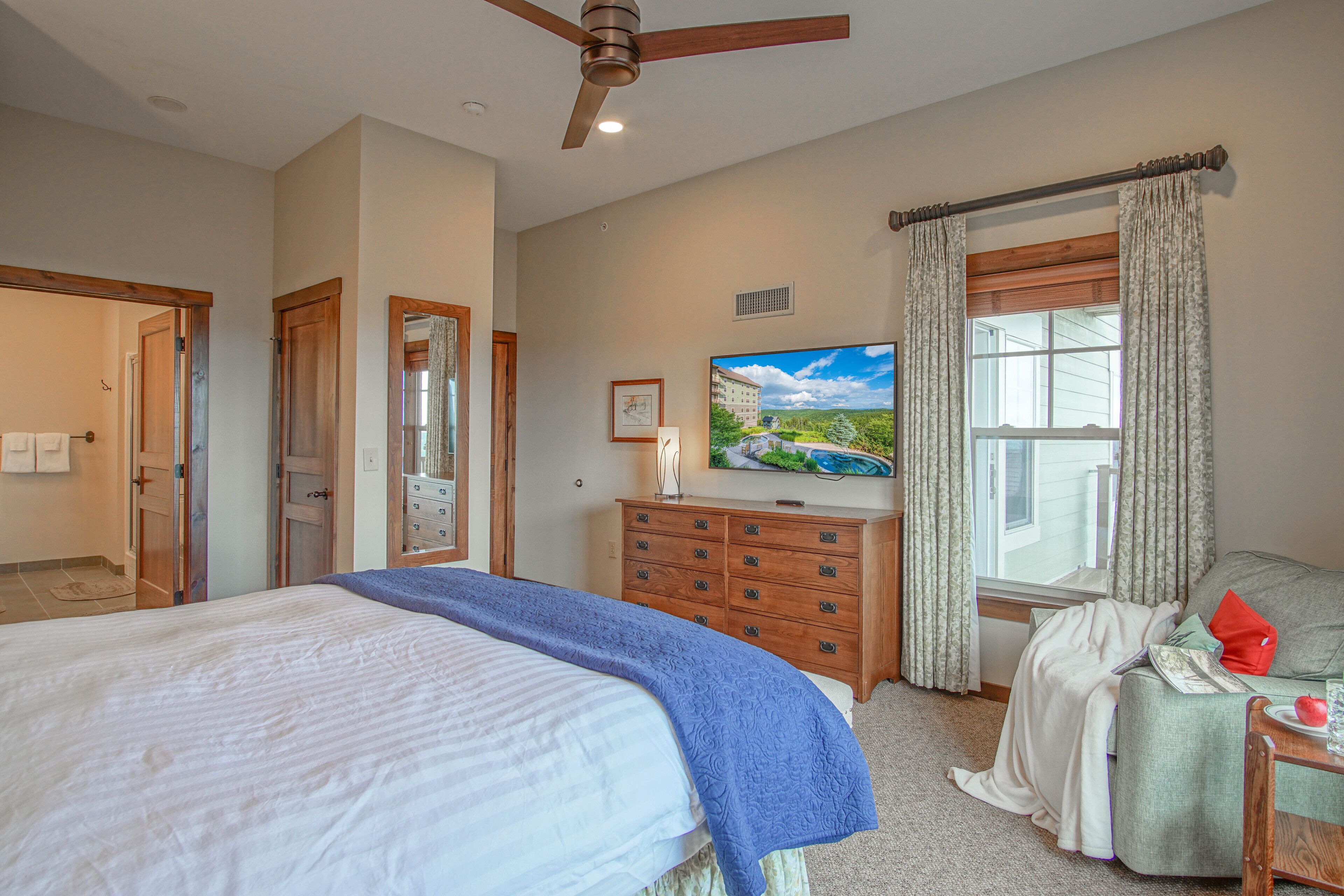 A bedroom with a bed, a dresser, a television, and a window with curtains.
