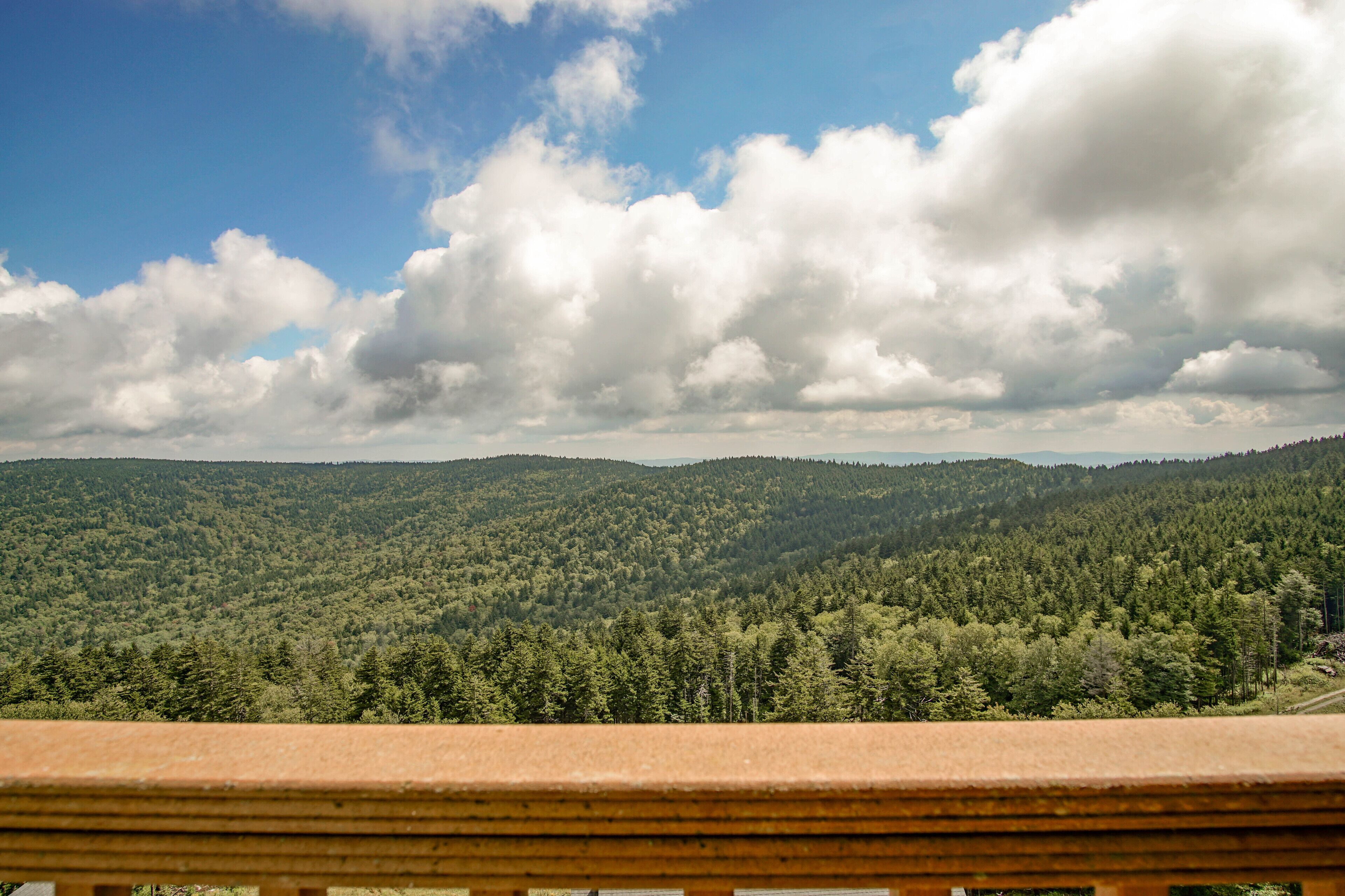 Ein weiter Panoramablick auf ein bewaldetes Gebirge mit einem Holzbalkon im Vordergrund.