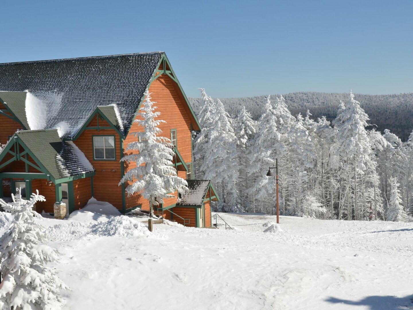 A wooden cabin with a sloped roof, surrounded by snow-covered trees and a clear sky.
