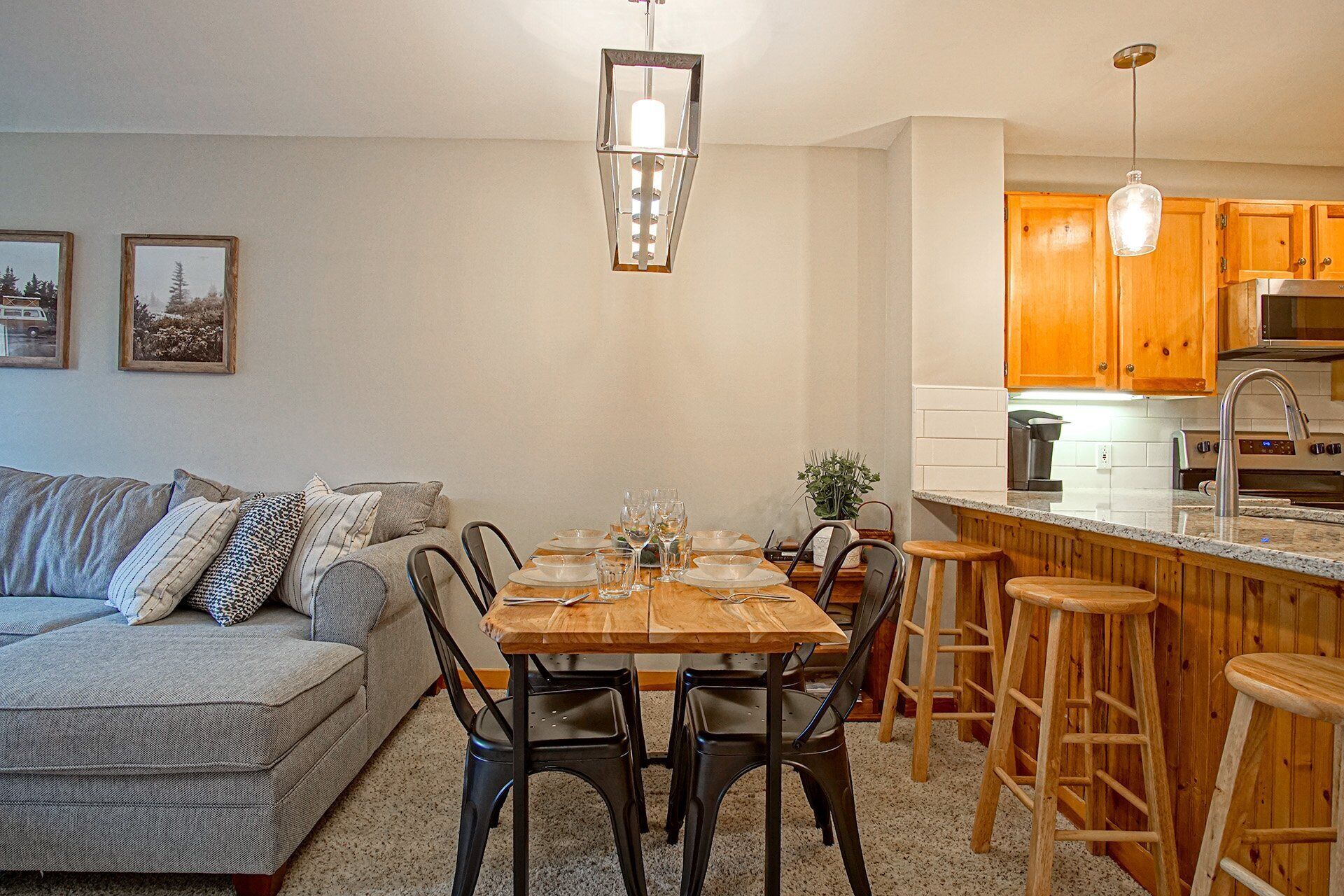Una sala de estar acogedora con un sofá, una mesa de comedor preparada para cuatro personas y una cocina con armarios de madera y un taburete de bar.