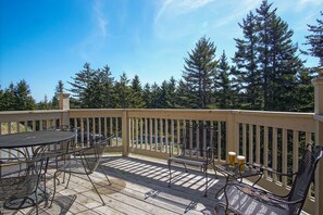 A wooden deck with metal furniture, including a table and chairs, and two glasses of beer. - Wabasso 4 is Gracefully Tucked in the Trees Between Central Village & South Mtn (Snowshoe)