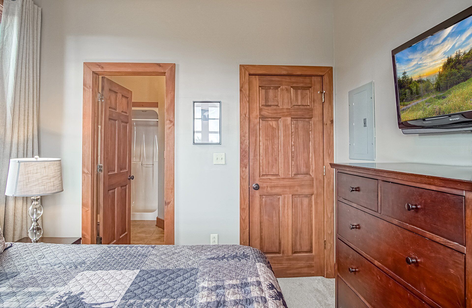 A bedroom with a bed, a dresser, a television, and two wooden doors leading to other rooms.